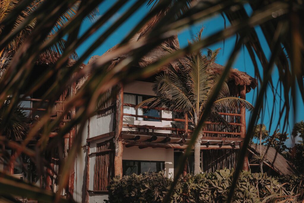 A two-story building with a balcony, surrounded by tropical vegetation.