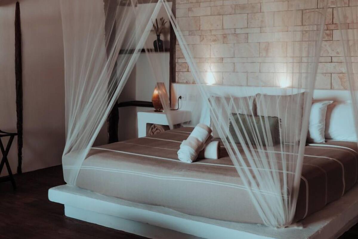 Una cama con dosel blanco y pared de ladrillo de fondo.