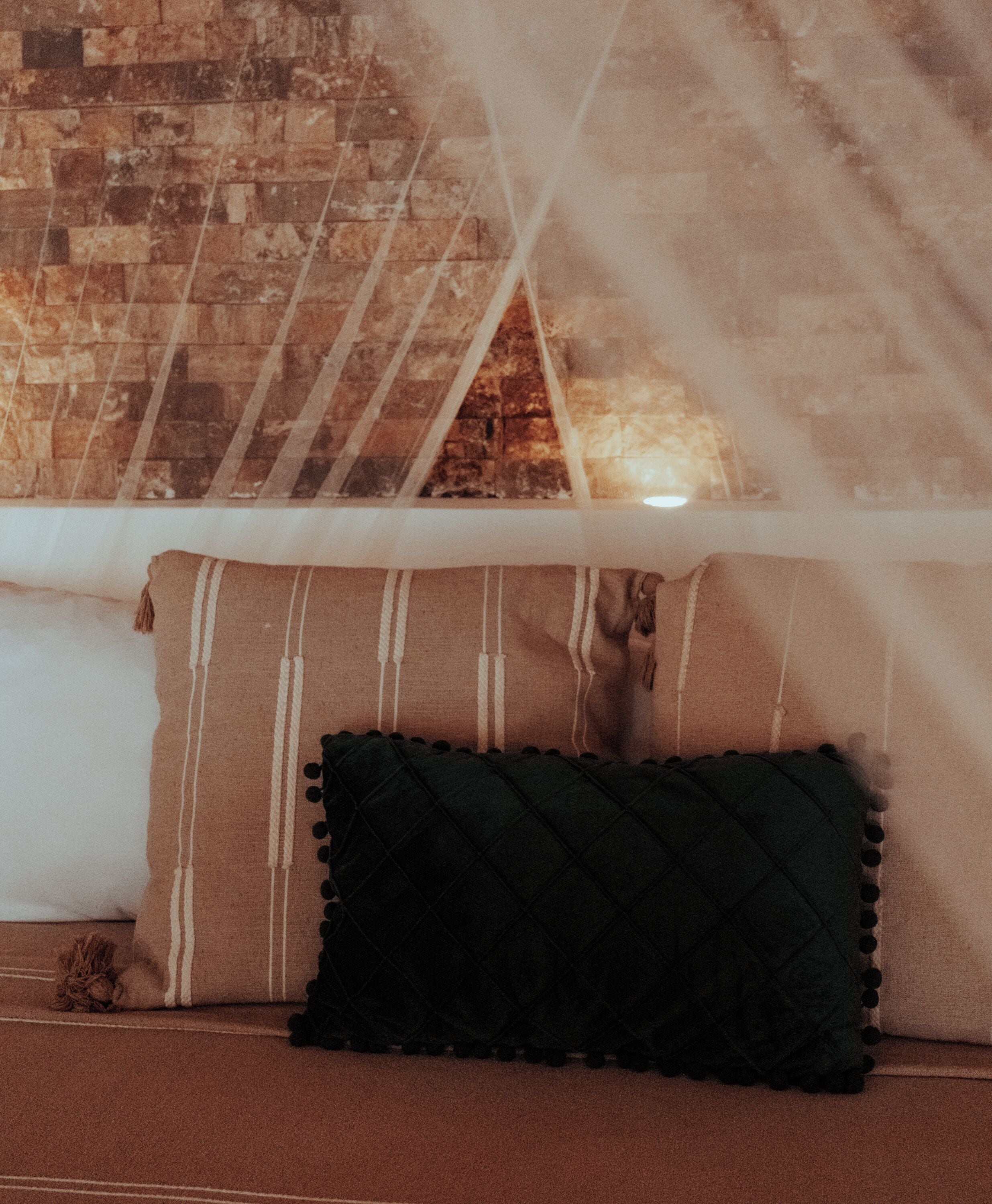 A bed with a striped pillow and a quilted pillow, a brick wall behind, and a sheer canopy.