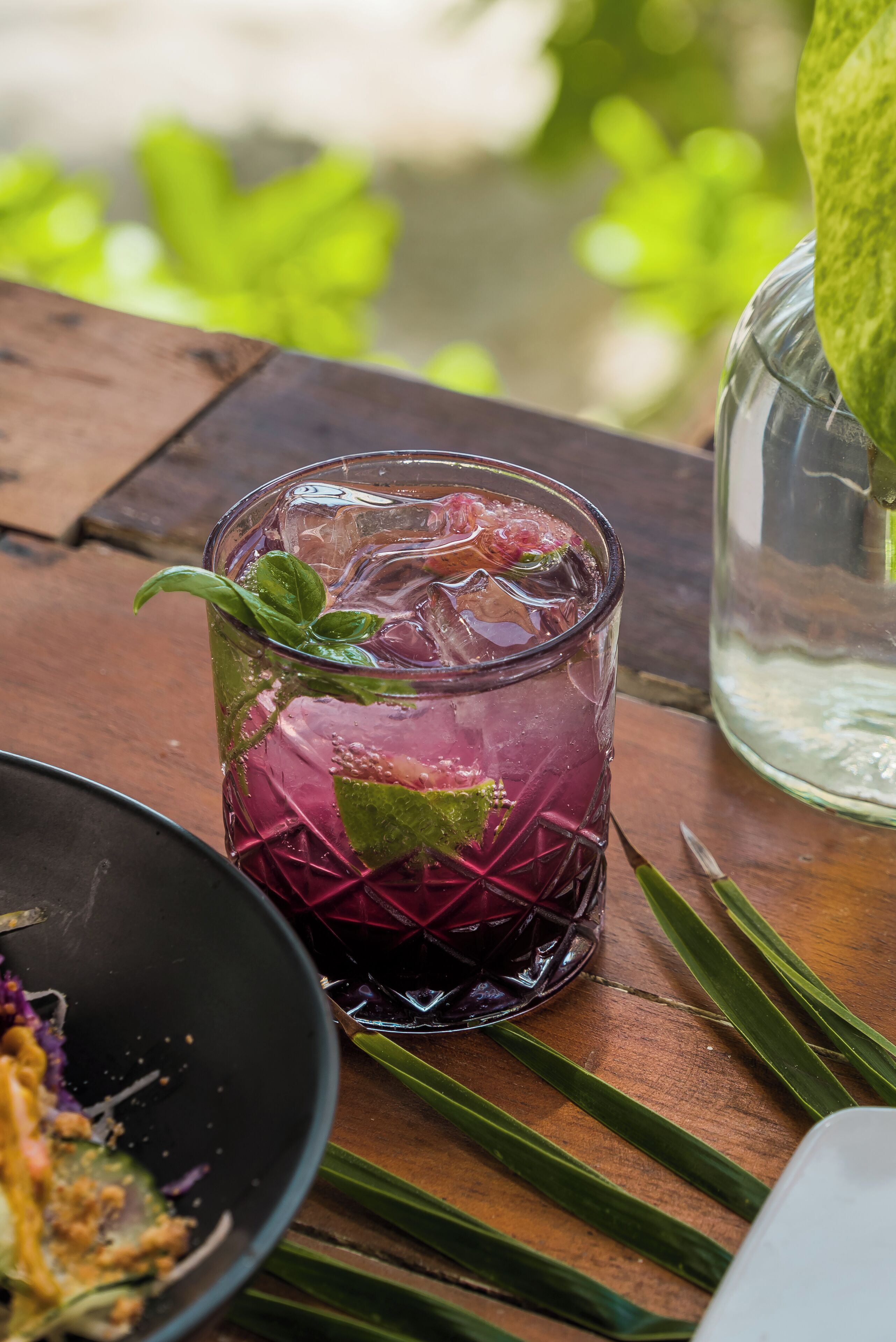 A glass of iced beverage with mint leaves, placed on a wooden table with a rustic setting.