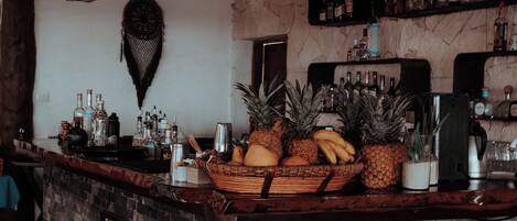 A bar area with a stone counter, wooden beams, and a variety of bottles and fruits.