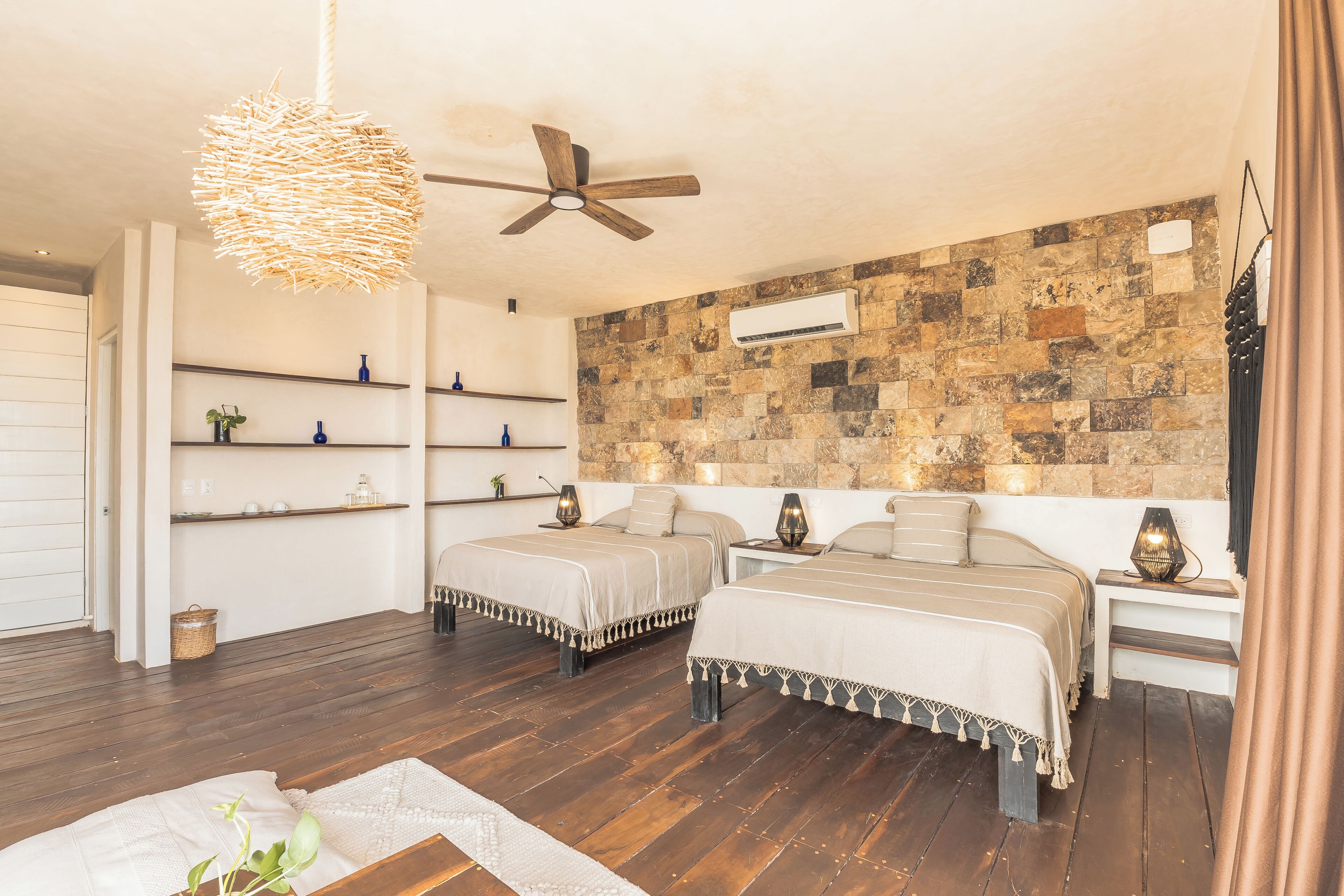 A bedroom with two beds, a stone wall, and a ceiling fan.