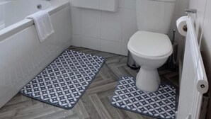 Ein modernes Badezimmer mit Badewanne, Toilette und Waschbecken. Zwei gemusterte Teppiche liegen auf dem Boden.