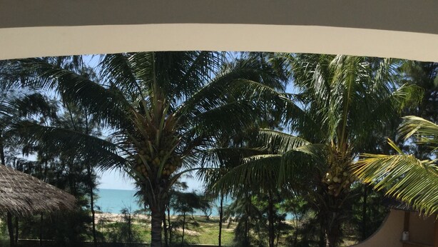 A swimming pool with lounge chairs and a thatched roof structure, surrounded by palm trees and a view of the sea. - Case Typique Sénégalaise Piscine vue mer (Palmarin)