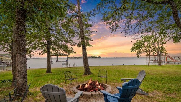 A lakeside outdoor seating area with Adirondack chairs and a fire pit, surrounded by trees and a view of the water. - Open Water~Sunsets~Swimming~Standing Work Station with High Speed Internet~Lake (Mabank)