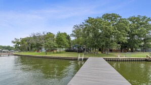 A wooden dock leading into a calm body of water, surrounded by trees and a small building with a green roof. - Open Water~Sunsets~Swimming~Standing Work Station with High Speed Internet~Lake (Mabank)