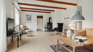 En hyggelig stue med pejs, træbjælker, spiseplads og sofa.