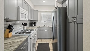 Una cocina compacta con armarios grises, cocina a gas, refrigerador y una ventana con persianas.