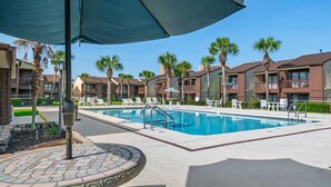 Una piscina con sillones de descanso y sombrillas, rodeada de edificios de varios pisos con balcones.