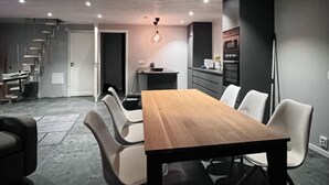 A modern dining area with a wooden table and white chairs, a staircase, and a kitchen in the background. - 1 bedroom awesome home in Hörby (Hörby)