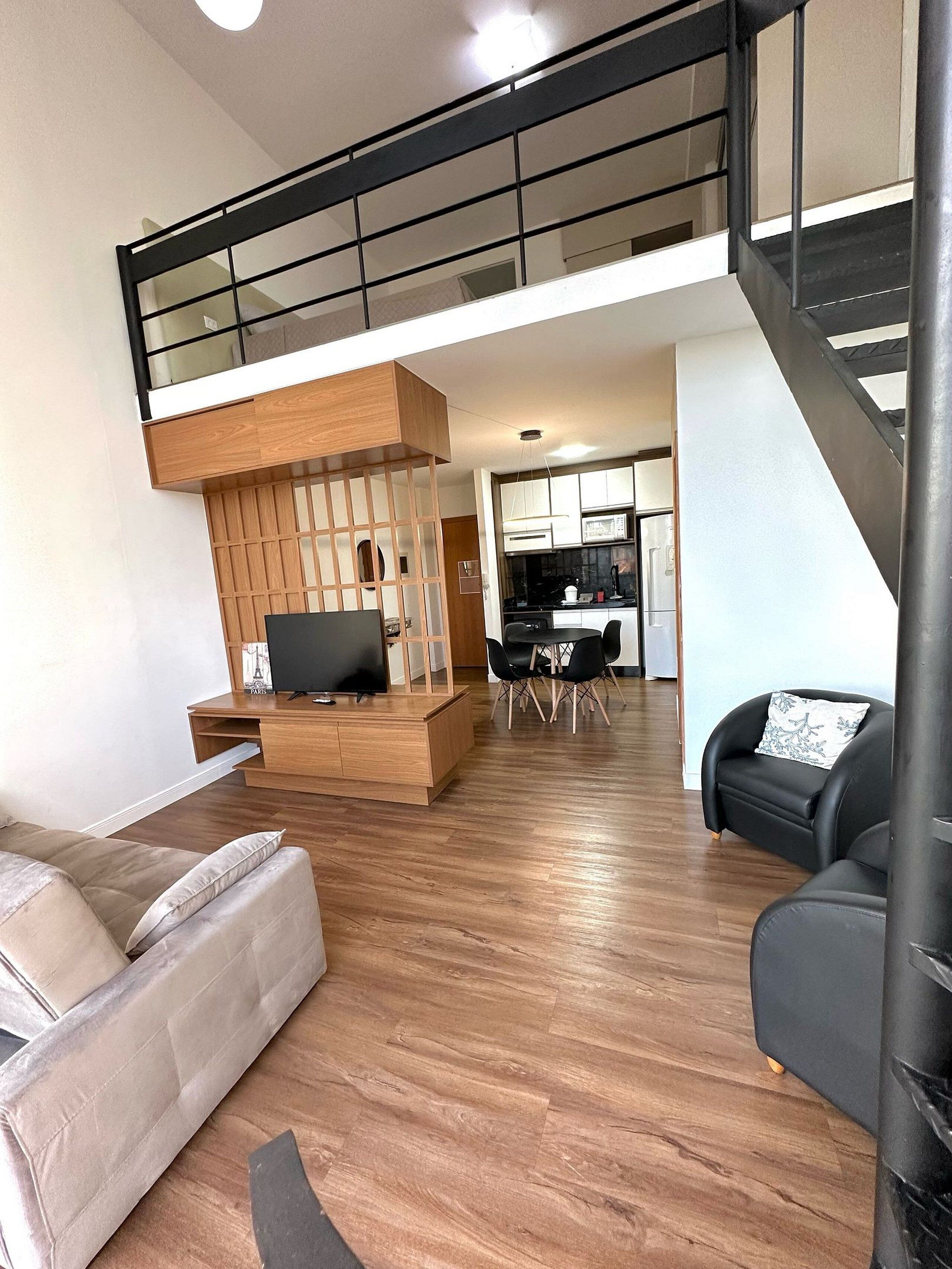 Una sala de estar moderna con un mueble de entretenimiento de madera, un sofá, un sillón negro y una zona de comedor con mesa y sillas.