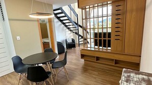 A modern interior with a wooden staircase, a dining area with a round table and chairs, and a large wooden cabinet with multiple drawers. - Saint Sebastian 307 Duplex no Centro. (Jaragua do Sul)