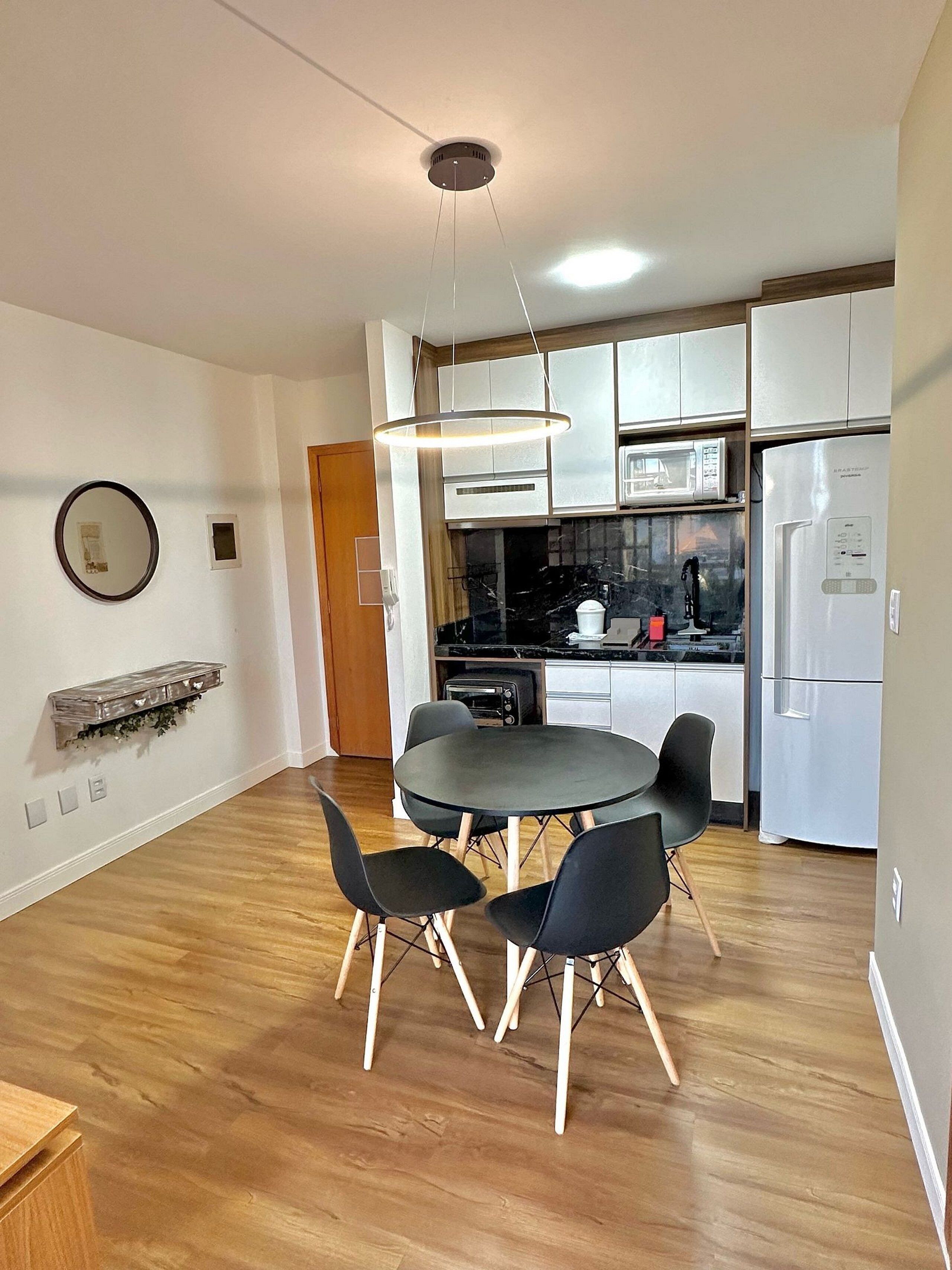 Een moderne keuken met witte kasten, een zwart aanrechtblad en een ingebouwde magnetron. Er staat een ronde eettafel met vier stoelen bij, met erboven een hanglamp.