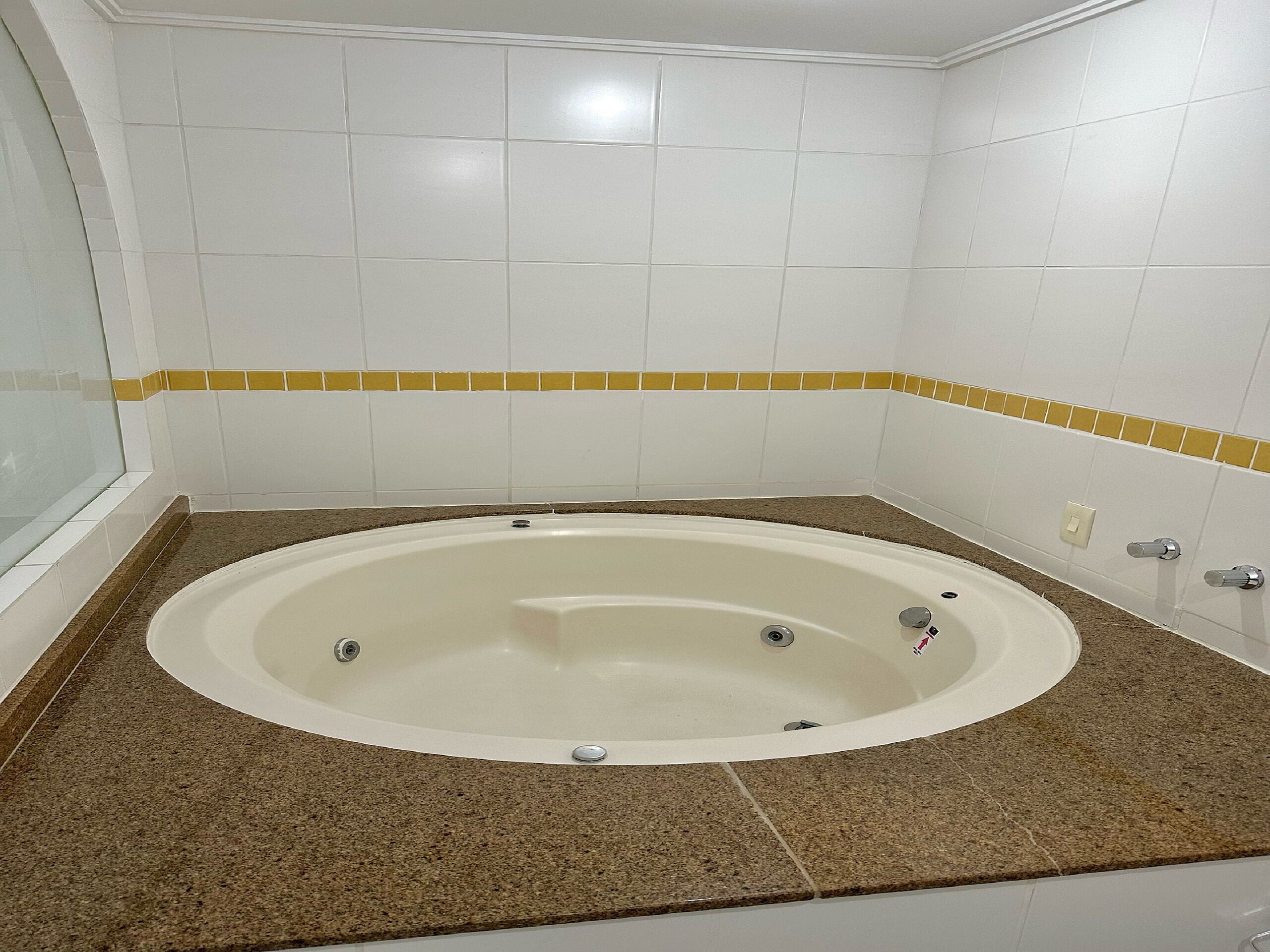 Un baño con una bañera independiente, paredes de azulejos blancos y encimera de granito marrón.