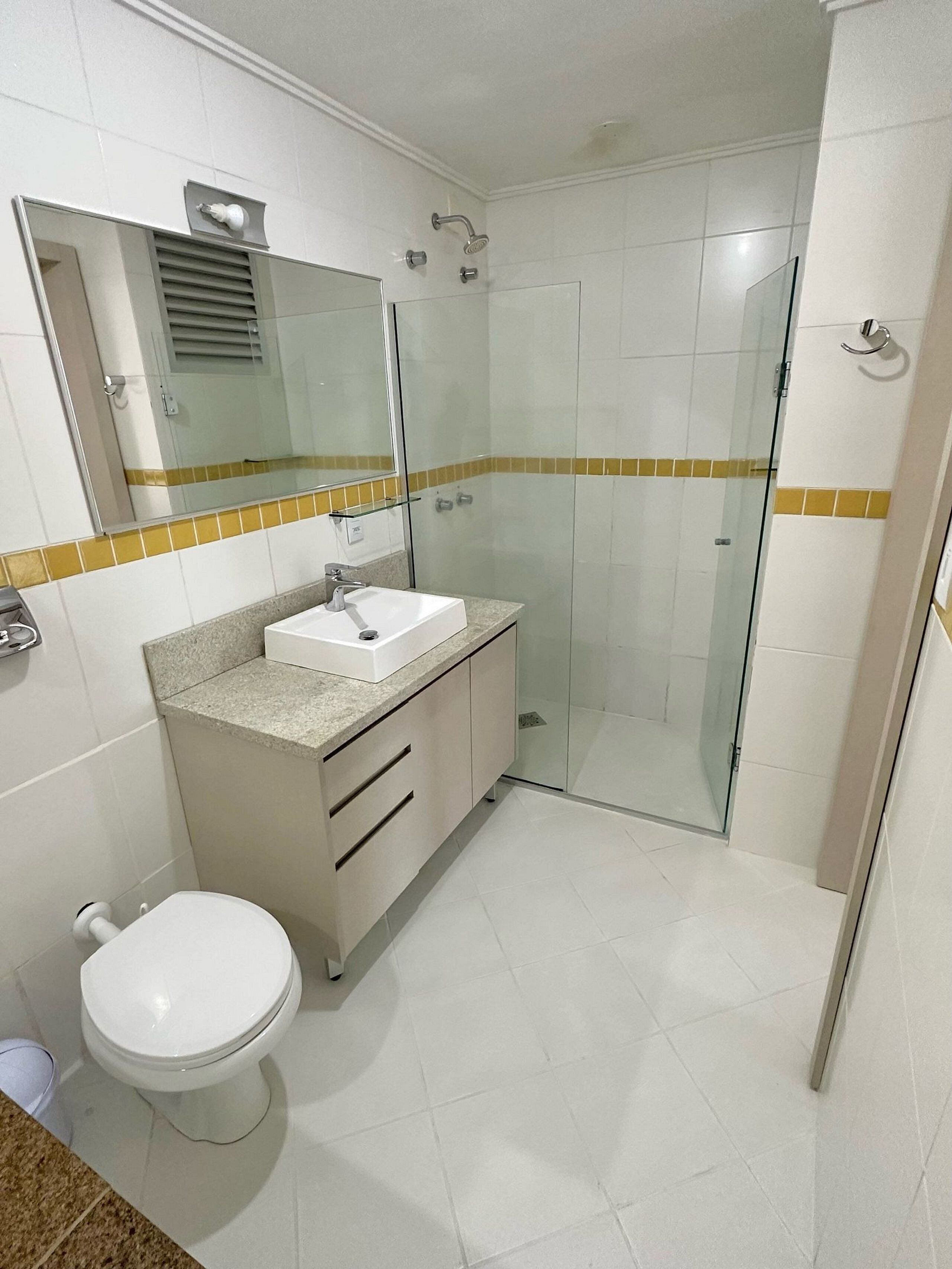 A modern bathroom with a white sink, mirror, and toilet. It features a glass shower enclosure and a tiled floor.