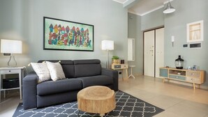 Un salón moderno con un sofá gris, una mesa de centro redonda de madera y un cuadro abstracto y colorido en la pared.