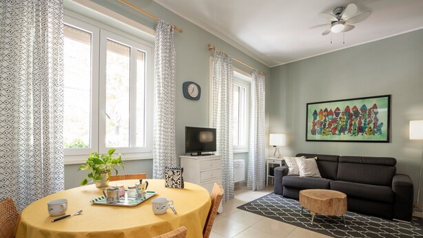 Un comedor con una mesa dispuesta para dos personas, un televisor, un sofá y un cuadro en la pared.
