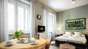Un dormitorio con cama, televisor, cuadro, mesita de noche y ventana con cortinas.