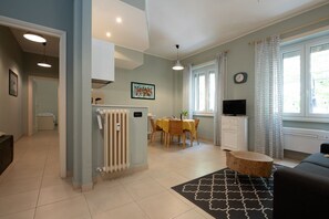 A modern living room with a sofa, a round wooden coffee table, a dining area with a yellow tablecloth, a radiator, and a TV. - Olimpico Apartment Flaminio (Roma)