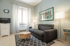 Un salon avec un canapé, une table basse, une lampe, un téléviseur et un tableau accroché au mur.