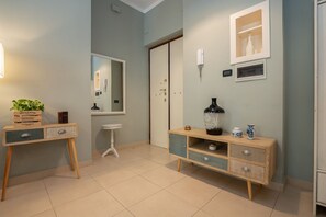 Una habitación con una consola de madera, un taburete blanco pequeño, un espejo y un mueble con adornos.