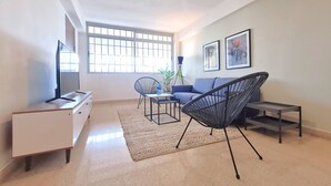 Ein Wohnzimmer mit Fernseher, Sofa, Sesseln und Bildern an der Wand.