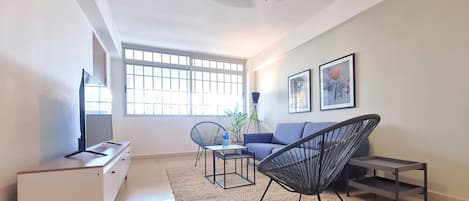 Una sala de estar con televisor, sofá, sillas y obras de arte en la pared.