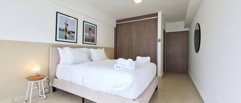 A neatly made bed with white linens, a small bedside table with a lamp, and two framed pictures on the wall.