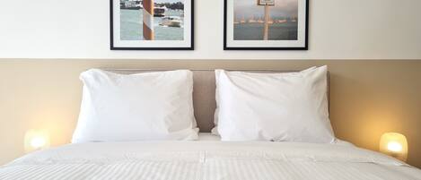 A hotel room with a bed, two framed pictures on the wall, and two bedside lamps.