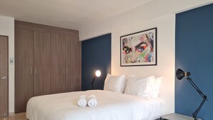 Ein Schlafzimmer mit Bett, Nachttisch, Lampe, Kleiderschrank und einem farbenfrohen Bild an der Wand.