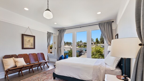 A spacious bedroom with a large bed, a bench with cushions, a patterned rug, and a view of the outdoors. - The McCann House Downtown Auburn 2 (Auburn)