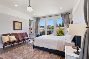 A spacious bedroom with a large bed, a bench with cushions, a patterned rug, and a view of the outdoors.