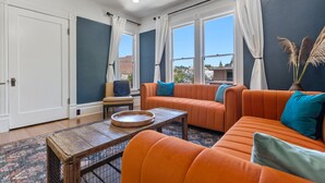 A living room with orange sofas, a wooden coffee table, and a view of the city through large windows. - The McCann House Downtown Auburn 2 (Auburn)