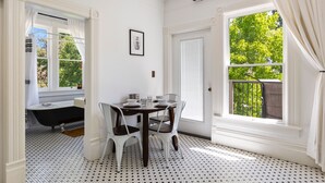 A room with a white and black patterned floor, a table with chairs, a bathtub, and a large window with a view of trees. - The McCann House Downtown Auburn 2 (Auburn)