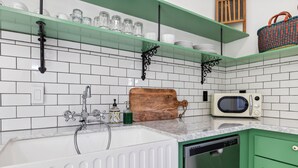 A kitchen with white subway tiles, a white sink, a microwave, and green cabinets. - The McCann House Downtown Auburn 2 (Auburn)