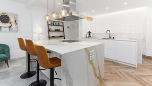 A modern kitchen with a marble island, pendant lights, and a built-in stove. - Magnífico Apartamento guadalmina baja  (Marbella)