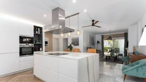 A modern kitchen with a central island, built-in oven, and pendant lighting. - Magnífico Apartamento guadalmina baja  (Marbella)