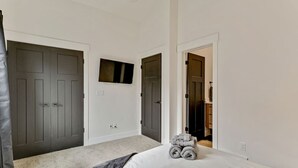 Un dormitorio con una cama, dos puertas, un ventanal pequeño y un baño visible a través de una de las puertas.