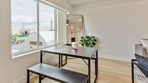 Una sala de estar moderna con un ventanal grande, una mesa de comedor, un banco, un sofá y una planta en maceta.