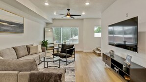Una sala de estar moderna con sofá, sillón, mesa de centro y televisor de pantalla plana montado en la pared.