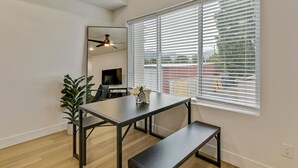 Una sala de estar moderna con una mesa de comedor, un banco y un amplio ventanal con persianas.