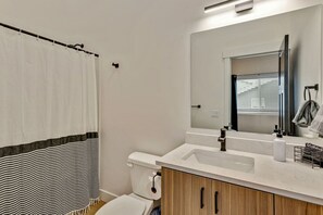 Un baño moderno con un lavamanos blanco, armarios de madera, un espejo grande y una cortina de ducha a rayas.