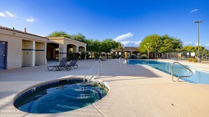 A swimming pool area with lounge chairs, a hot tub, and a covered patio with a building in the background.