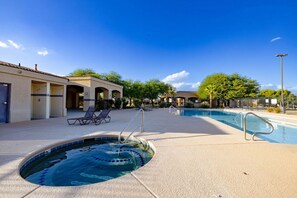 Un espace piscine comprenant des chaises longues, un jacuzzi et un patio couvert, avec un bâtiment visible en arrière-plan.