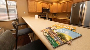 A kitchen with wooden cabinets, a stainless steel refrigerator, and a bar stool.