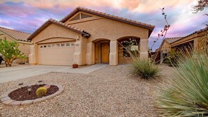 A single-story house with a garage, a driveway, and a gravel front yard with plants.