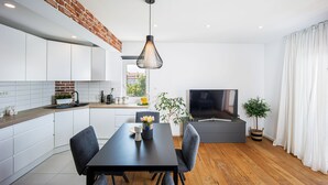 Una cocina moderna con armarios blancos, una pared de acento de ladrillo y una zona de comedor con una mesa y sillas oscuras.