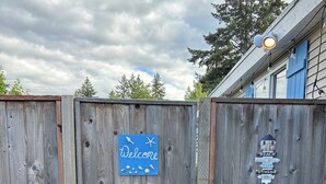 Ein hölzernes Tor mit einem 'Welcome'-Schild, einem kleinen Haus-Symbol und einem Schild, das 'Strandhausordnung' auflistet, zusammen mit Wörtern wie 'entspannen', 'erholen' und 'genießen'.