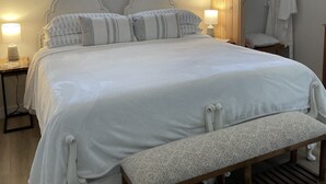 Ein Schlafzimmer mit einem großen Bett, Nachttischlampen, einem Fenster und einer hölzernen Sitzbank.