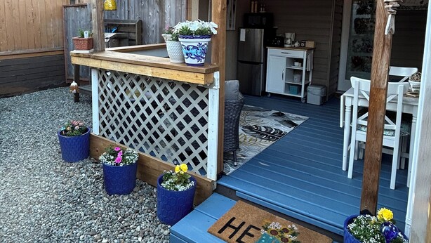 Eine überdachte Terrasse mit Holzdeck, Kübelpflanzen, einer Fußmatte und Lichterketten.